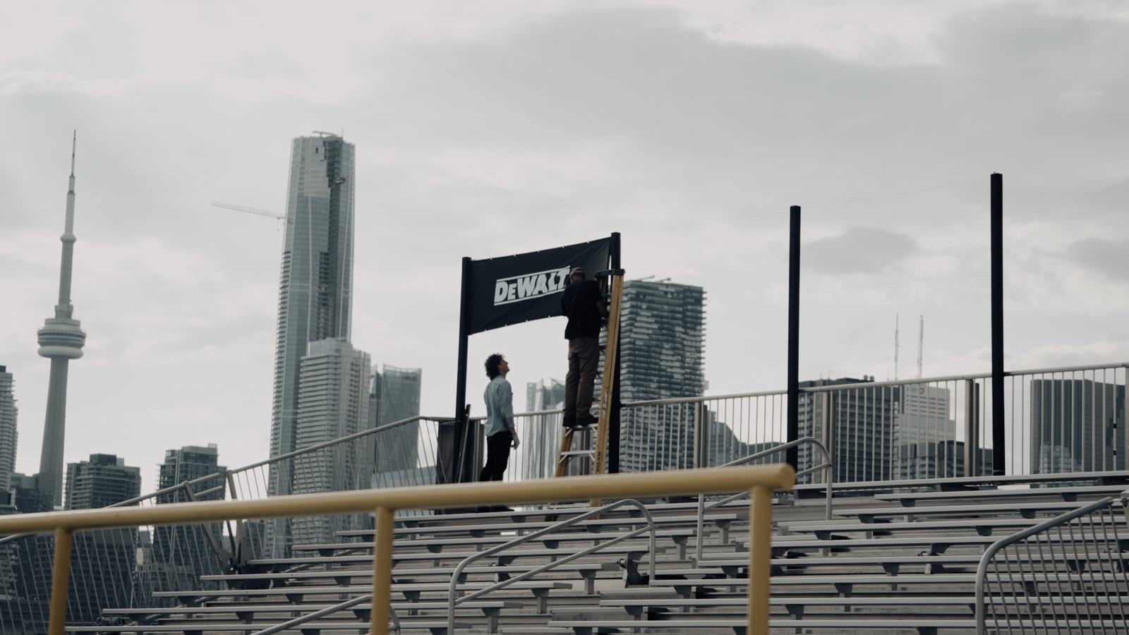 Crew hanging a DEWALT banner above the bleachers, CN Tower behind