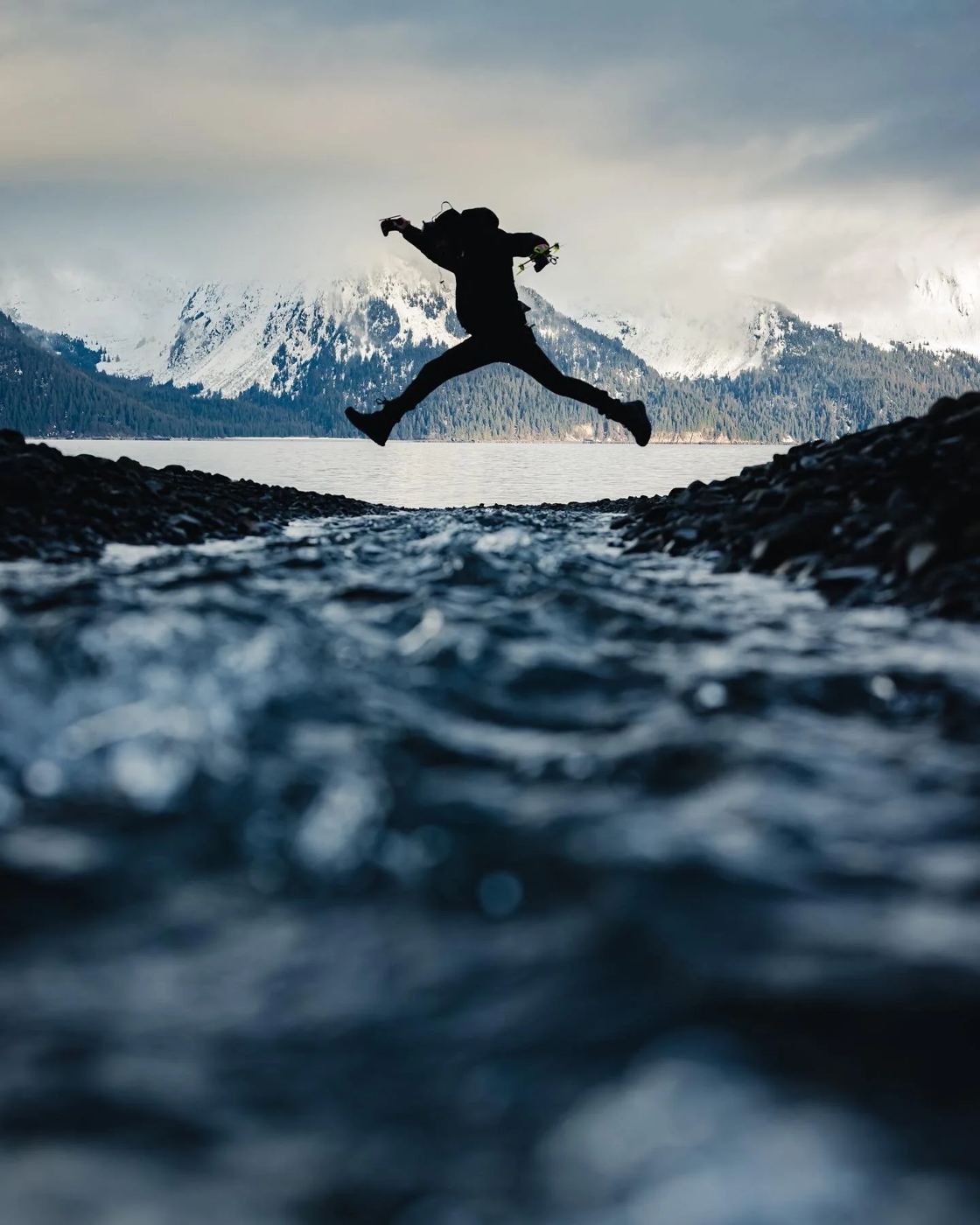 Spencer mid-leap over a glacier stream, FPV drone in hand