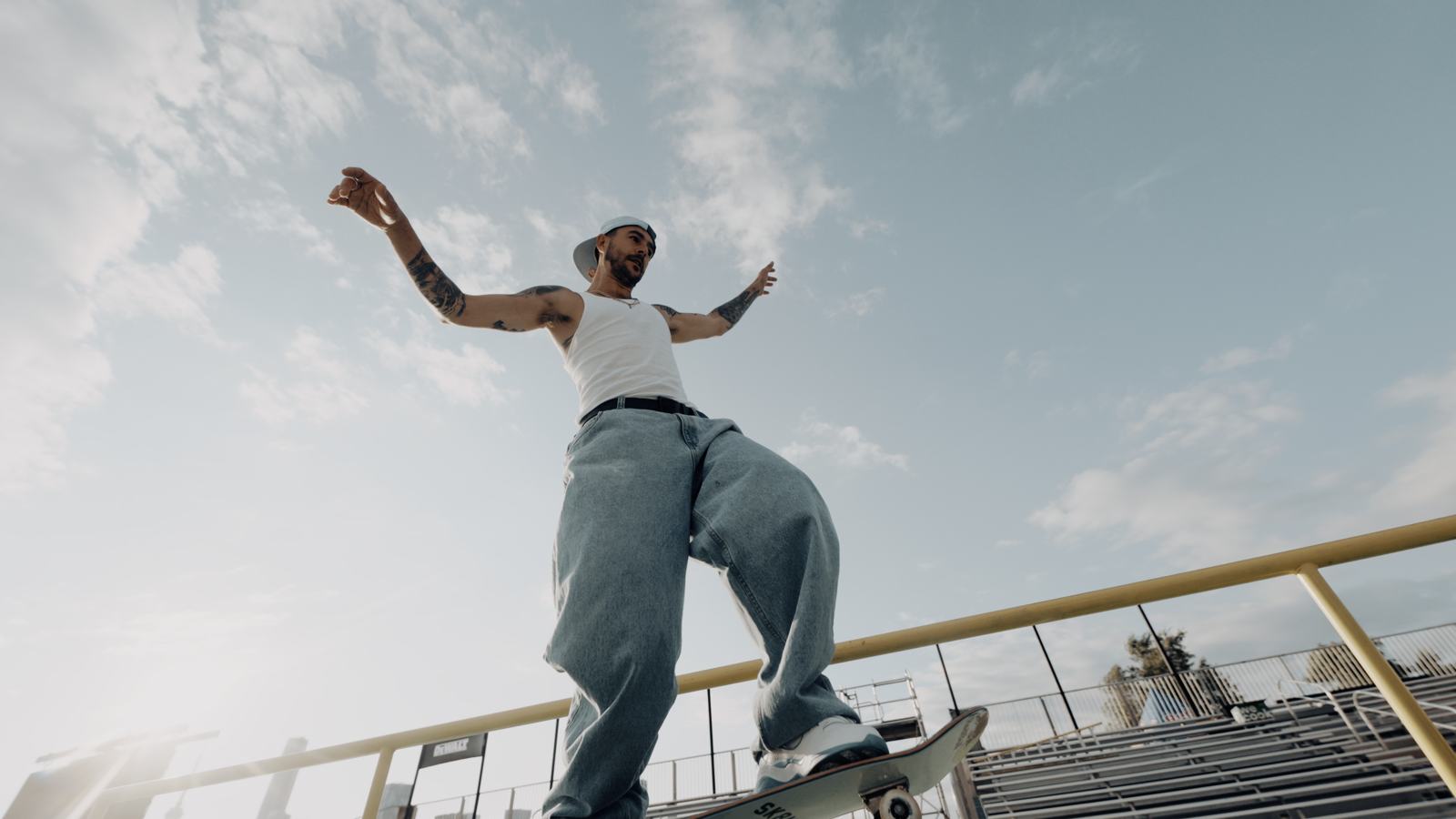 Tattooed skater balancing on a rail, shot from below